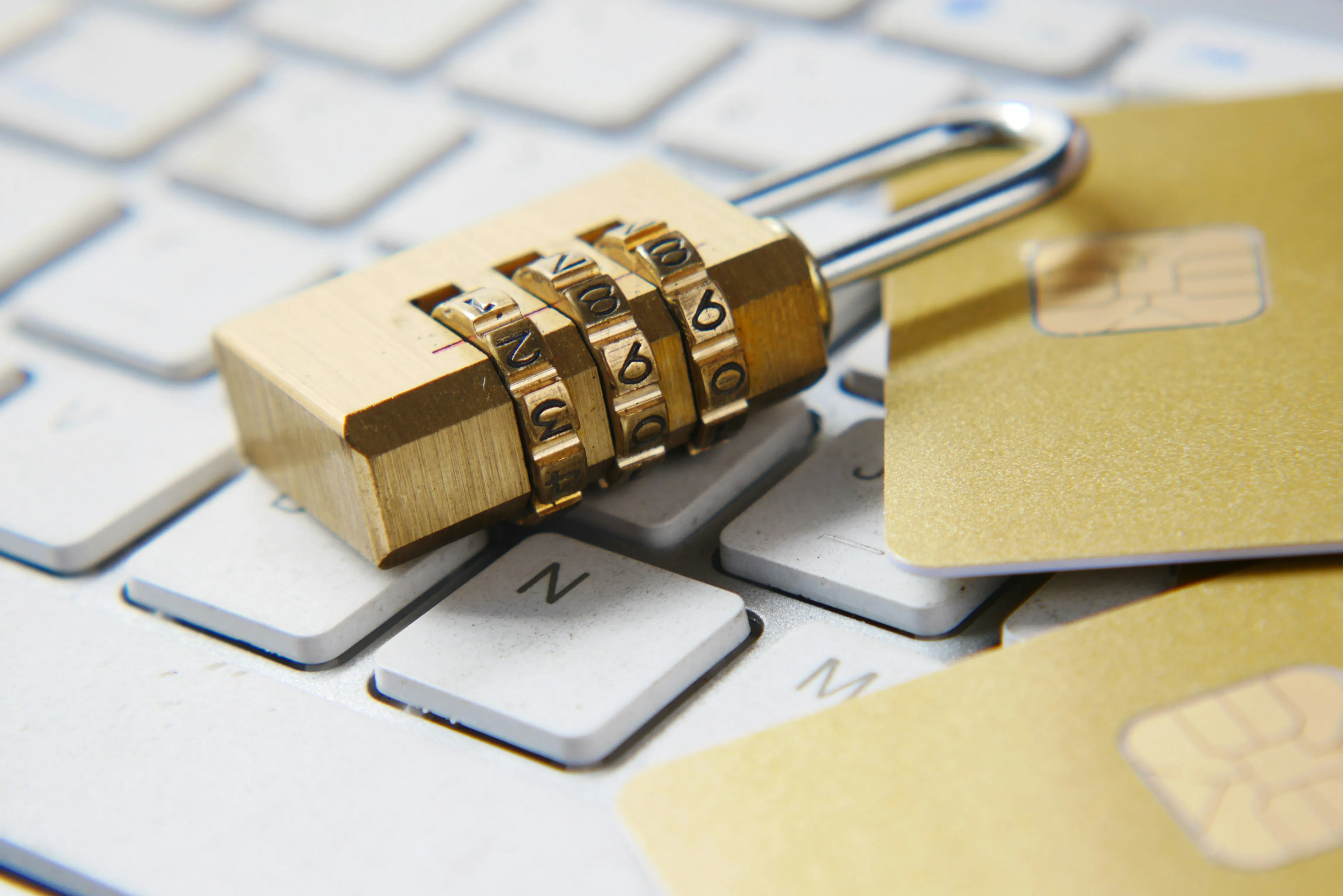 A physical lock laying on a laptop keyboard next to some credit cards, symbolizing privacy and security in the digital realm.